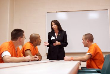 Three inmates listen to a woman discuss options and privileges that they might earn while serving time in prison.